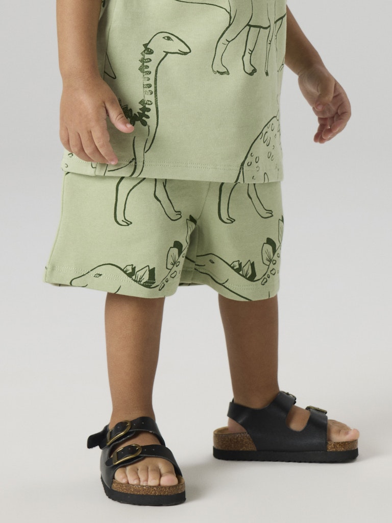 Child wearing a green outfit with dinosaur prints on a plain background