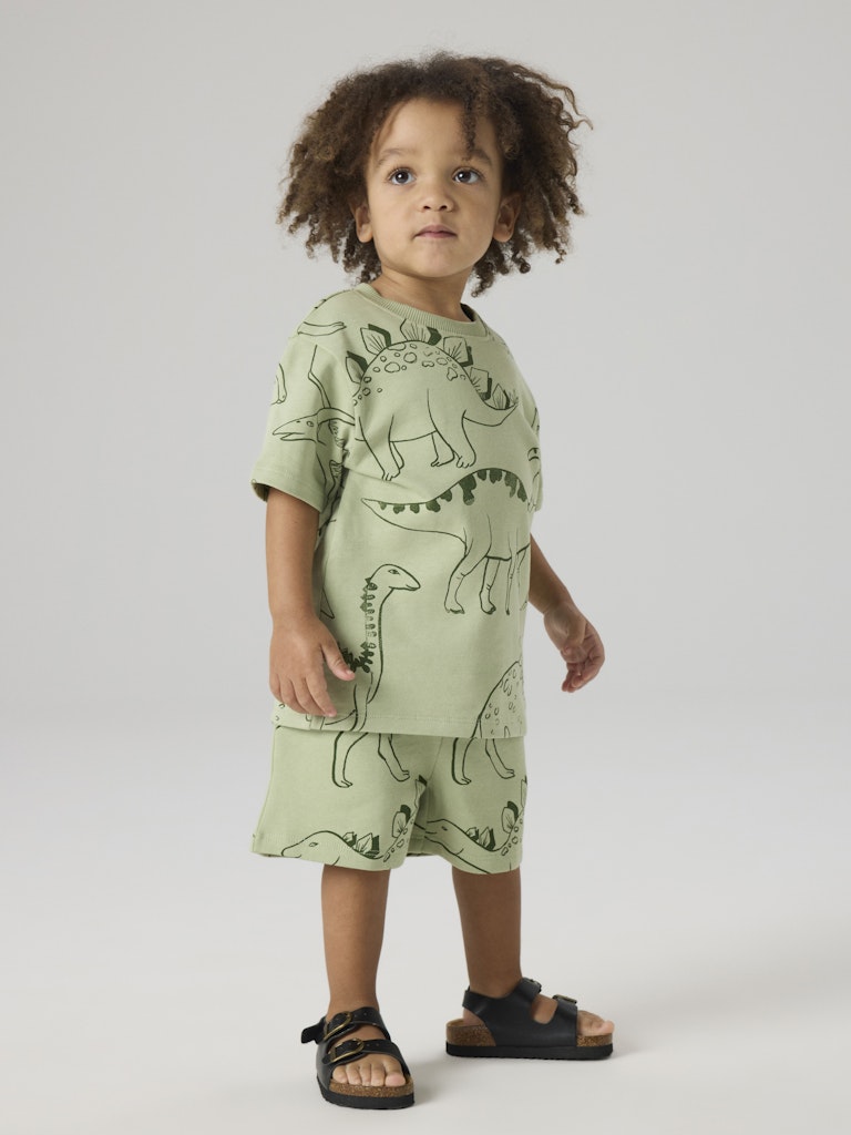 Child wearing a green outfit with dinosaur prints on a white background