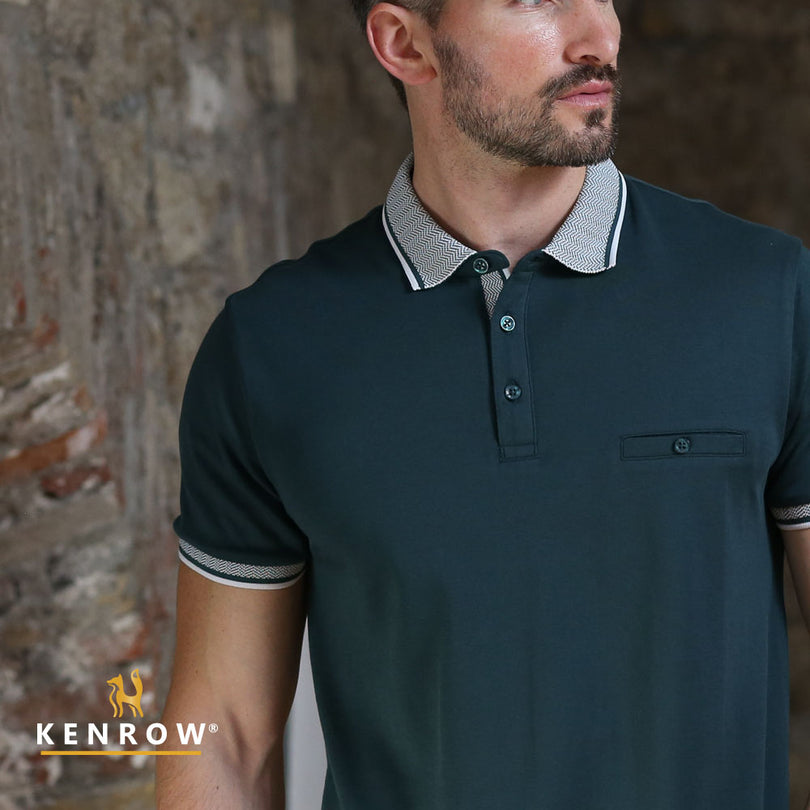 Man wearing a dark green polo shirt with striped sleeves against a stone wall, featuring the brand 'Kenrow'.