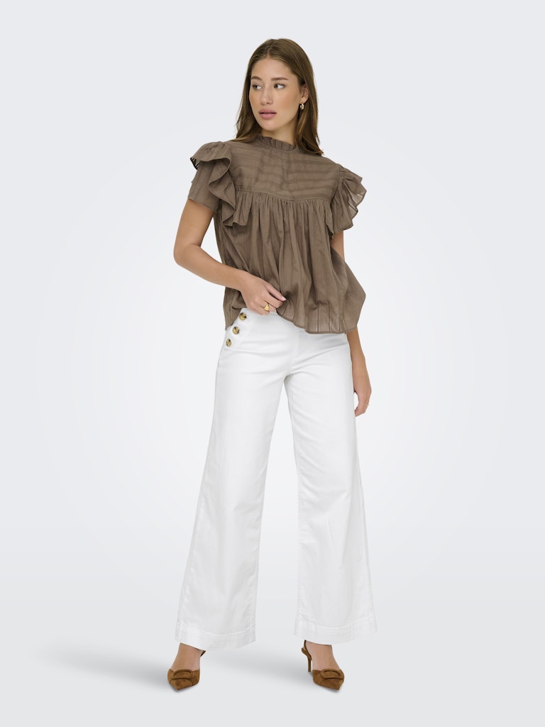 Woman wearing a brown ruffled blouse and white pants on a white background