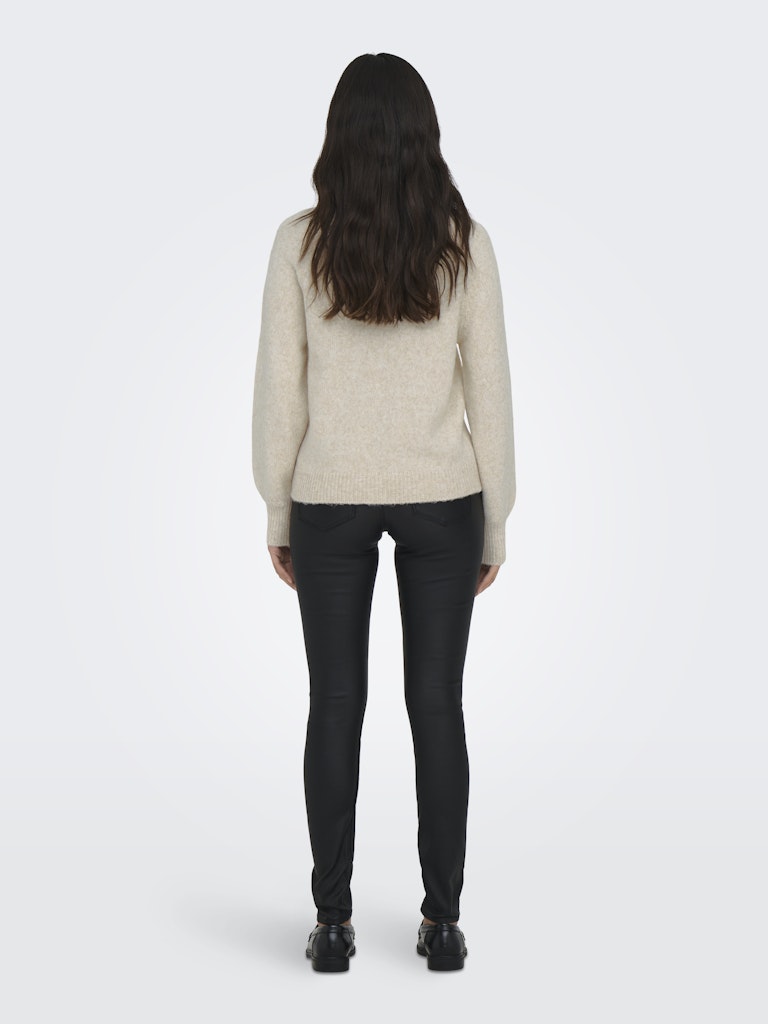 Person wearing a beige sweater and black pants on a white background