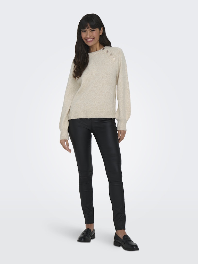 Woman wearing a beige sweater and black pants on a white background