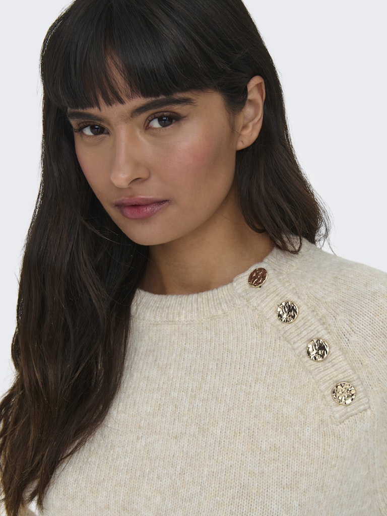 Woman wearing a beige sweater with decorative buttons on a white background