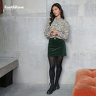 Woman in floral top and green skirt standing against a concrete wall with 'Rant&Rave' branding.