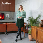 Woman in a green patterned shirt and dark green skirt standing in a modern living room with 'Rant&Rave' branding.