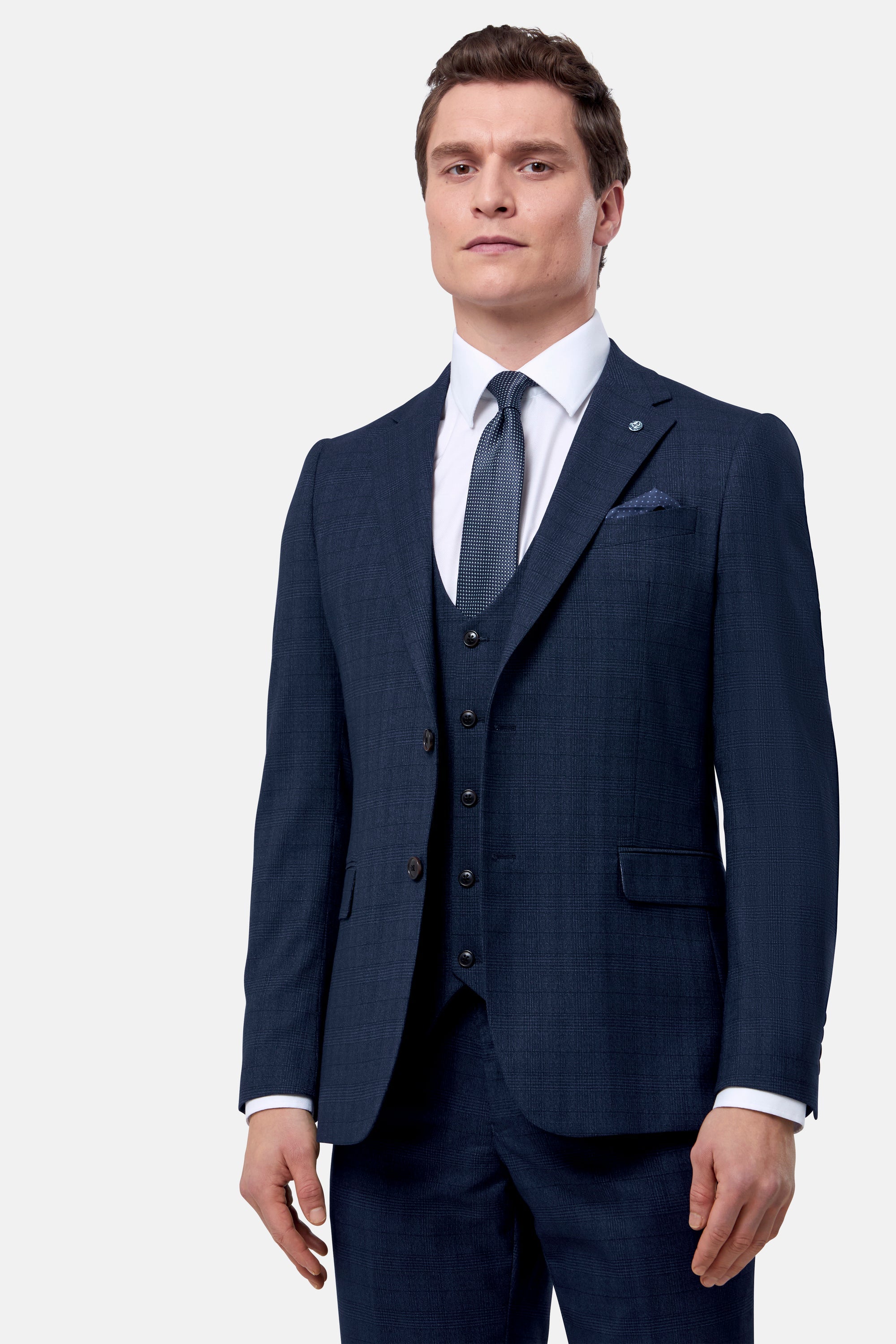 Man wearing a navy blue check jacket and waistcoat with a white shirt and tie on a light gray background