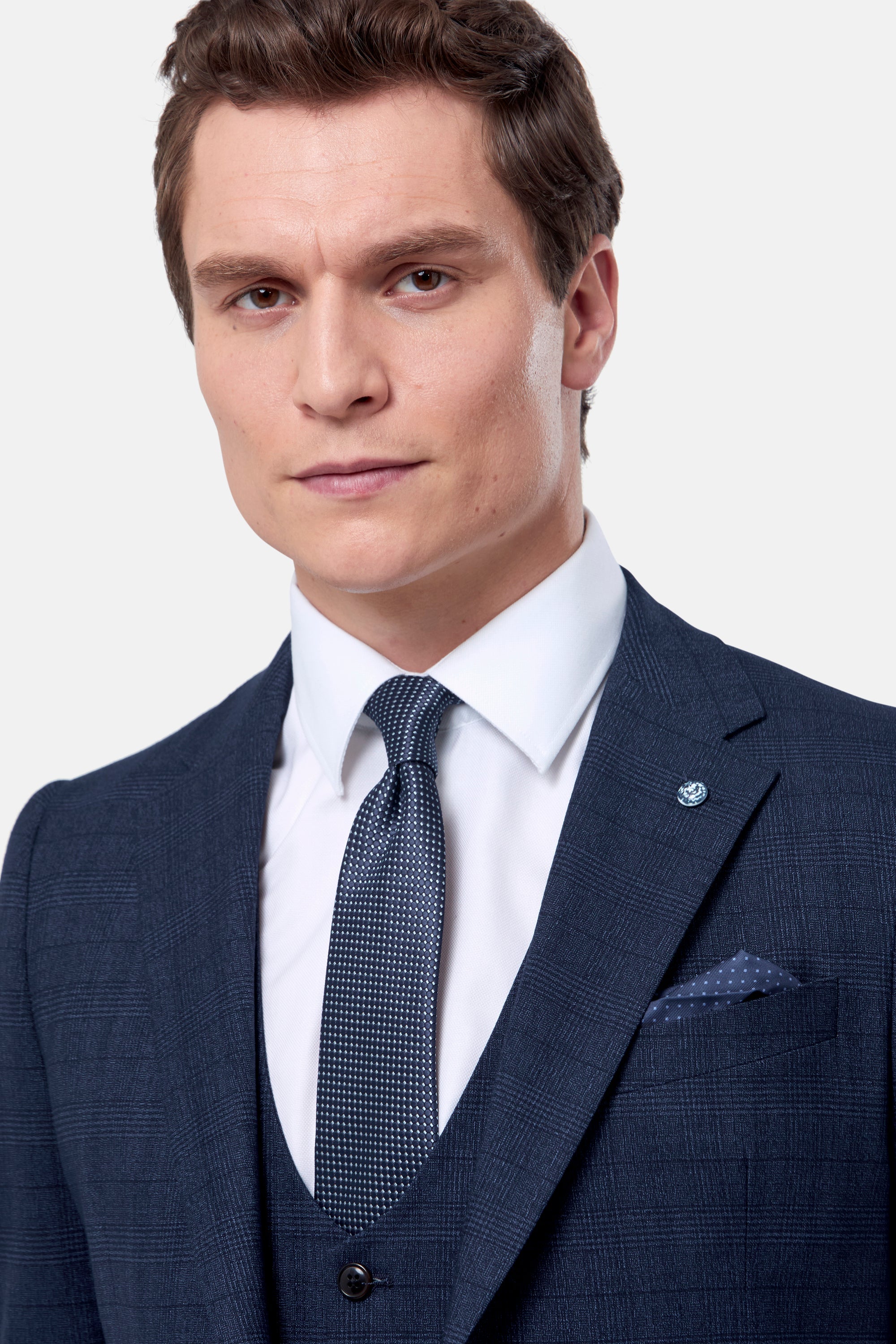 Man wearing a blue jacket and waistcoat with a white shirt and patterned tie on a light background