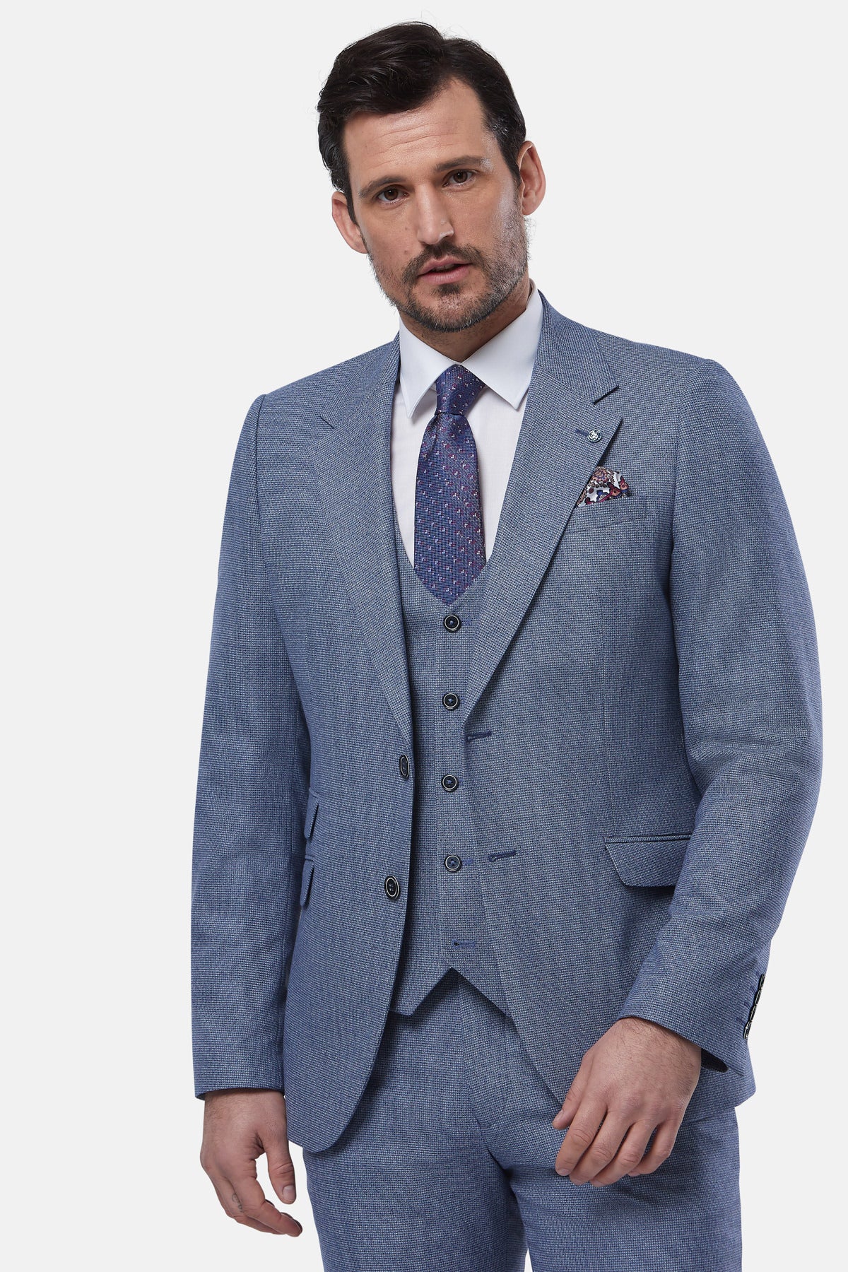 Man wearing a blue suit with a white shirt and patterned tie on a light gray background