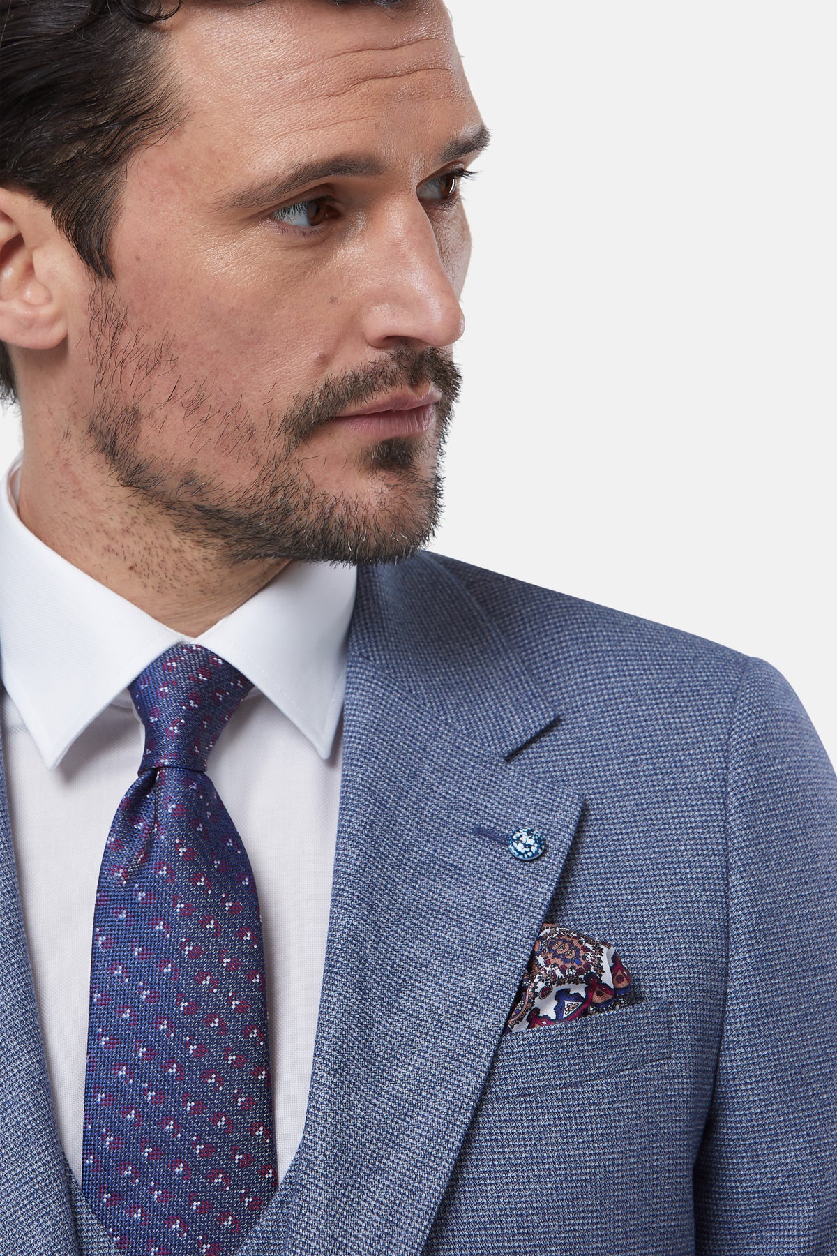 Man wearing a blue suit with a patterned tie and pocket square on a light gray background