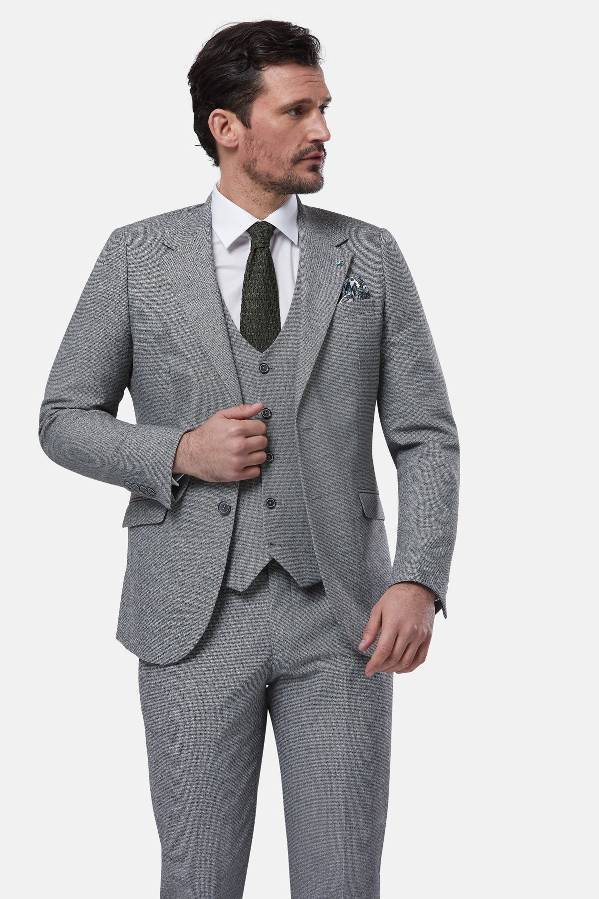 Man wearing a gray suit with a white shirt and patterned tie on a light gray background