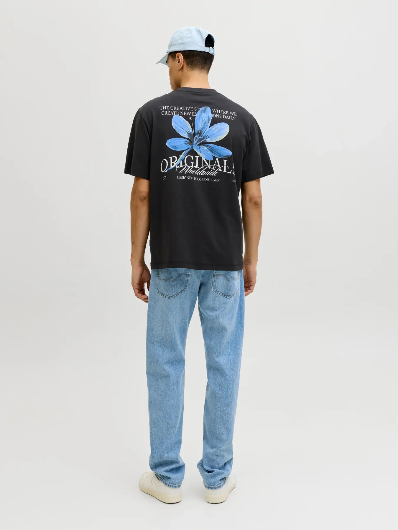 Person wearing a black t-shirt with a blue flower design and light blue jeans on a white background