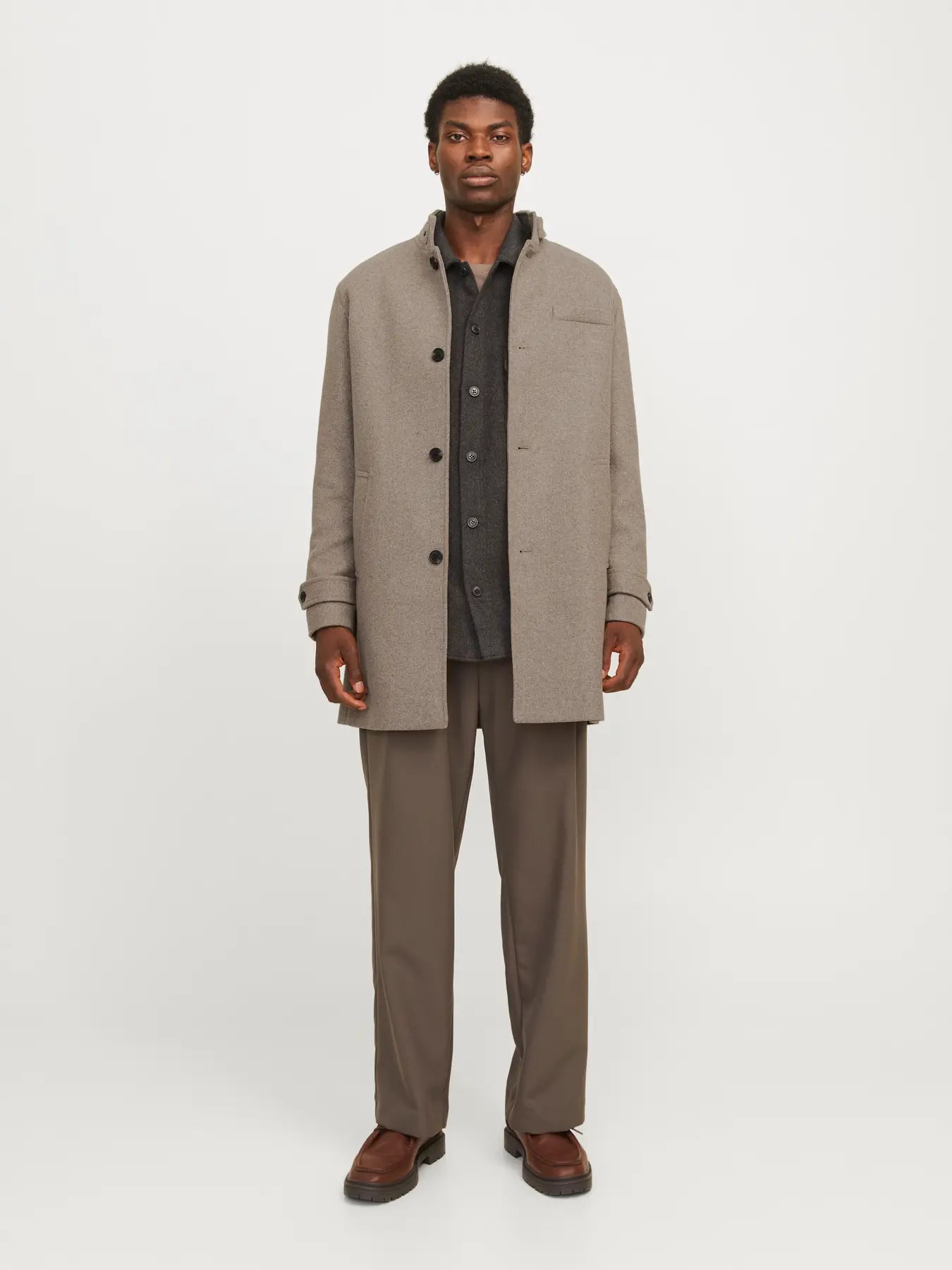 Man wearing a beige overcoat and brown pants on a white background