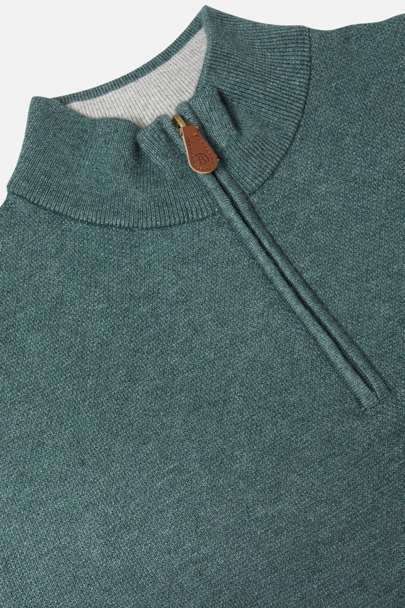 Close-up of a teal sweater with a zipper and brown tag on a white background