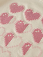 A close-up of a light cream fabric printed with pink pixelated ghost motifs, featuring a subtle glitter texture.