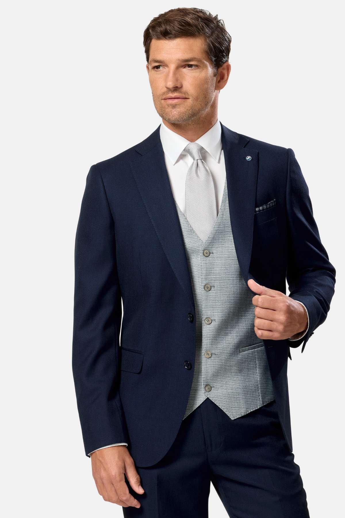 Man wearing a navy suit, sage waistcoat with a white shirt and patterned tie on a light gray background