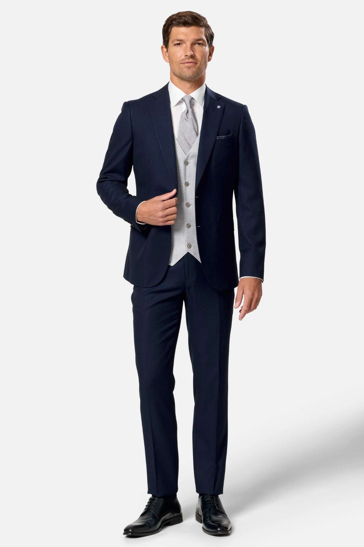 Man wearing a navy suit with a white shirt and patterned tie on a light gray background