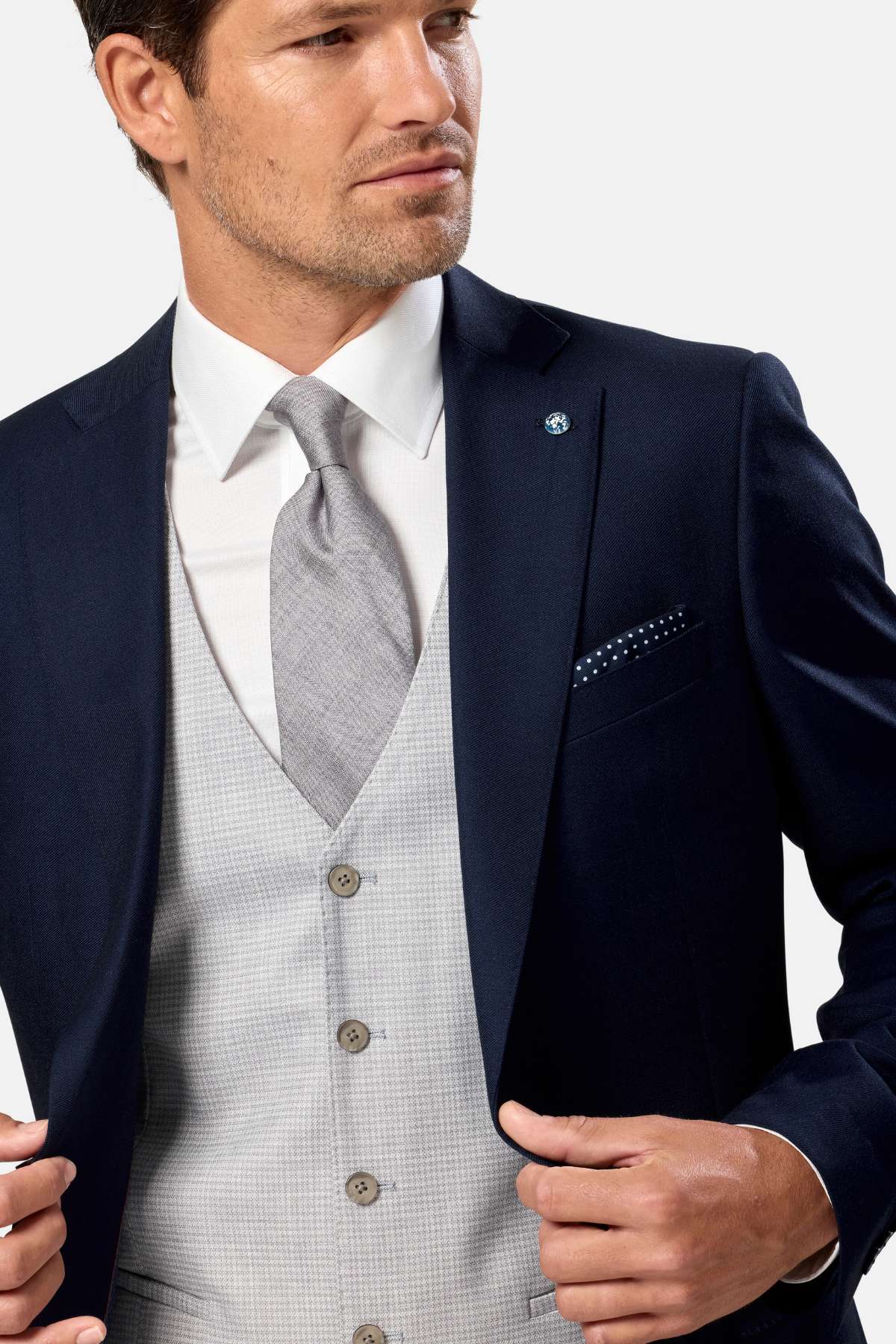 Man wearing a navy blazer, white shirt, and gray waistcoat against a white background