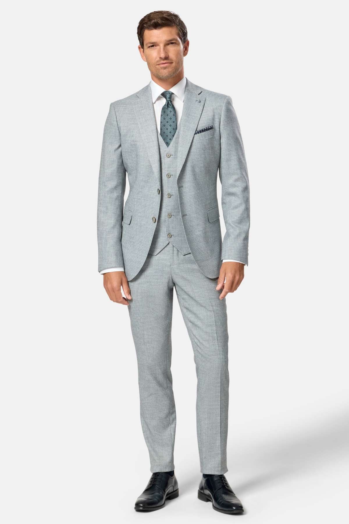 Man wearing a sage green suit with a white shirt and dark shoes on a white background