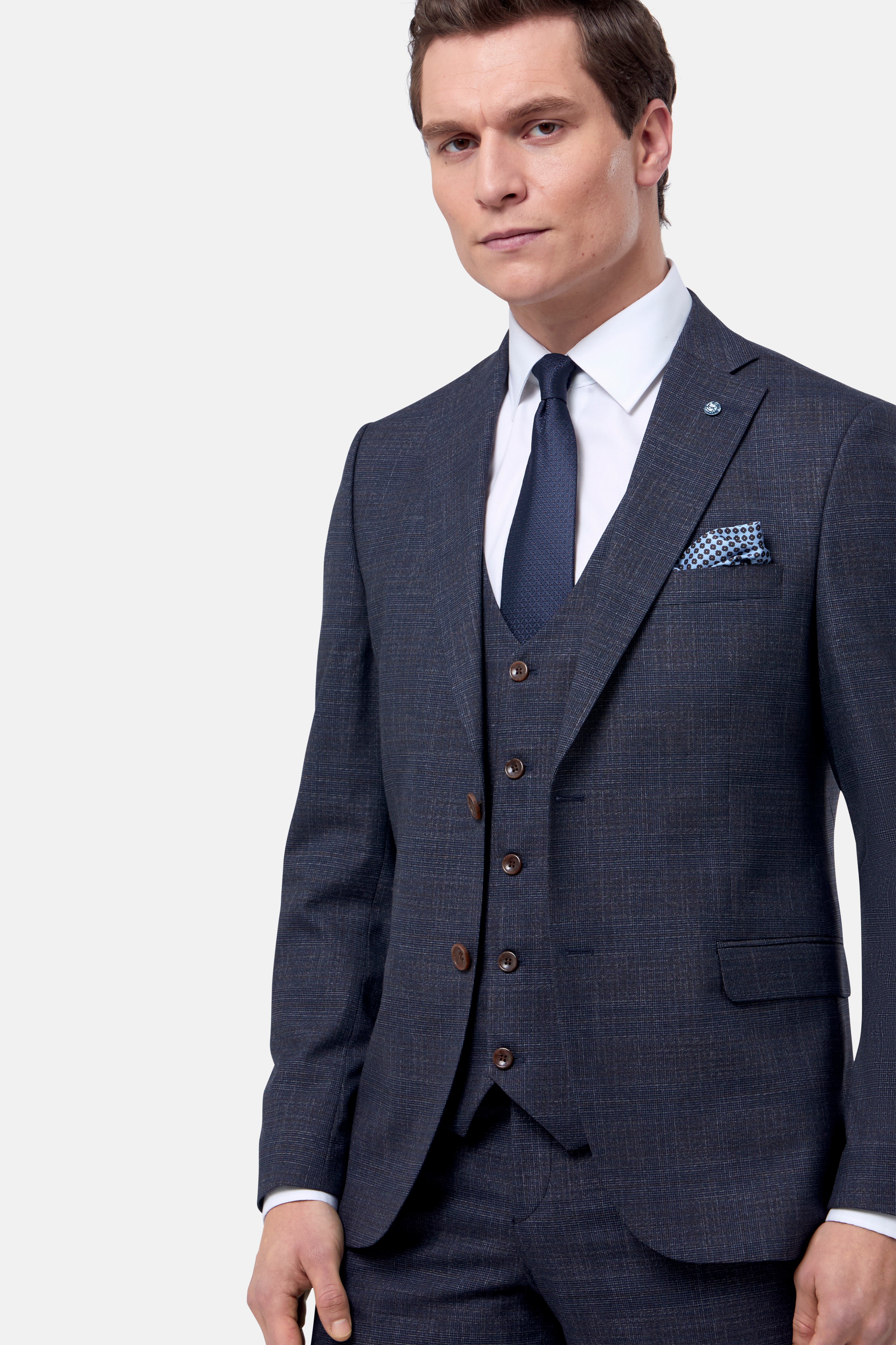 Man wearing a navy & brown check suit with a white shirt and blue tie on a light gray background