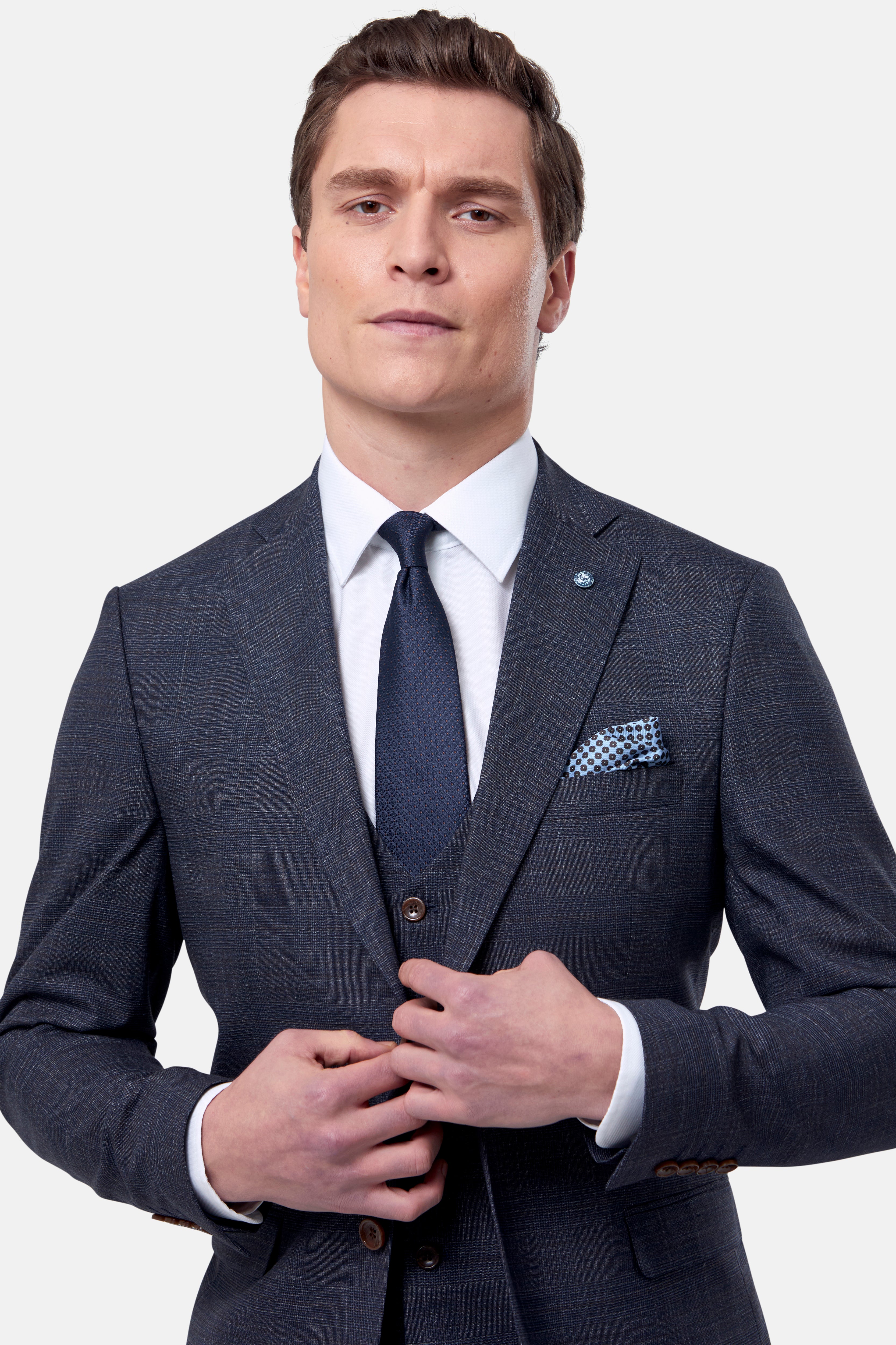 Man wearing a navy & brown check suit with a white shirt and tie on a light gray background