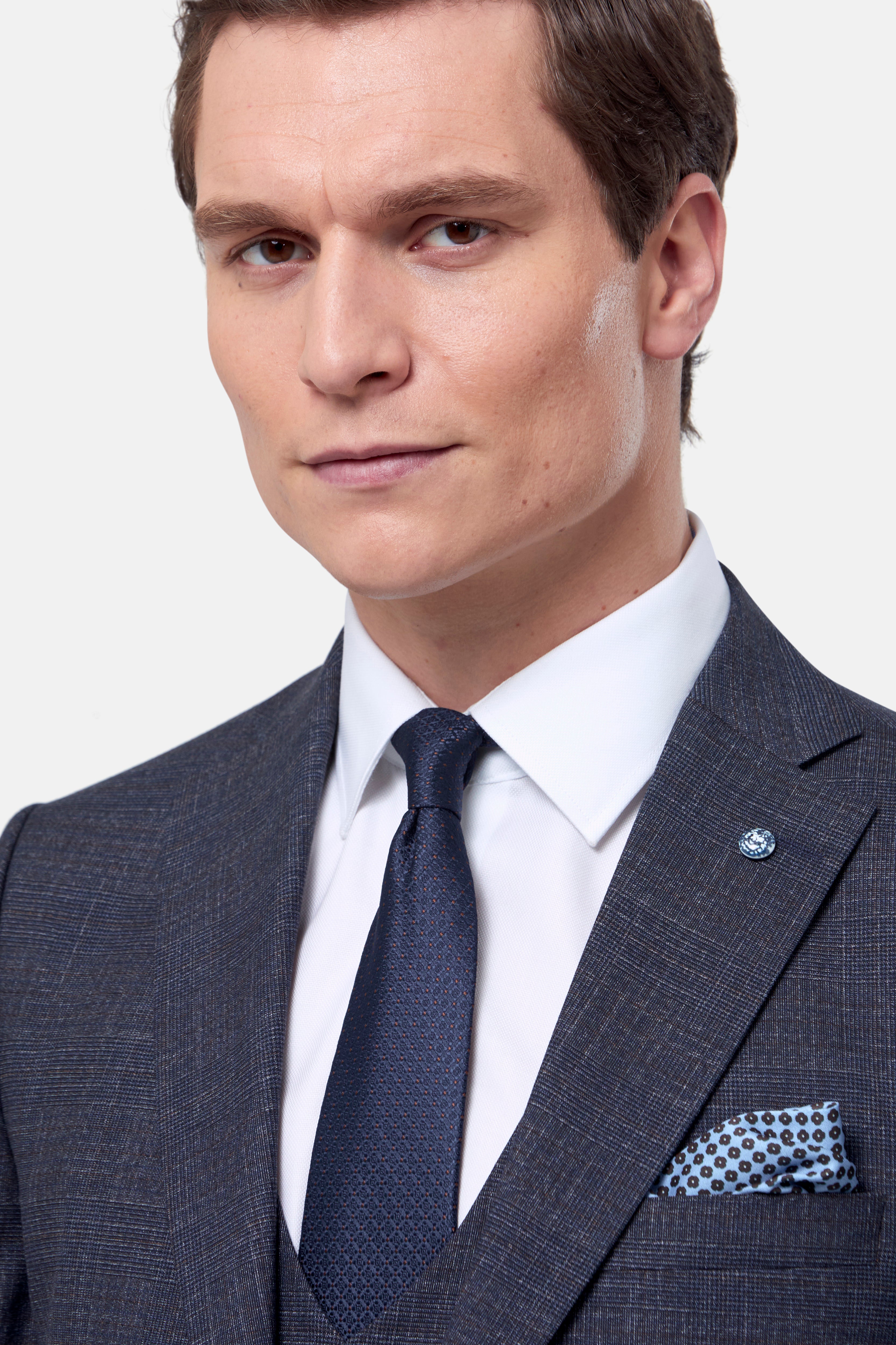 Man wearing a navy & brown check suit with a white shirt and patterned tie on a light gray background
