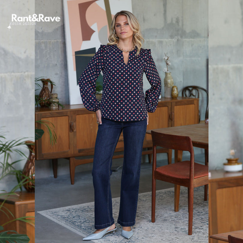 Woman wearing a polka dot blouse and jeans standing in a room with wooden furniture and decor.