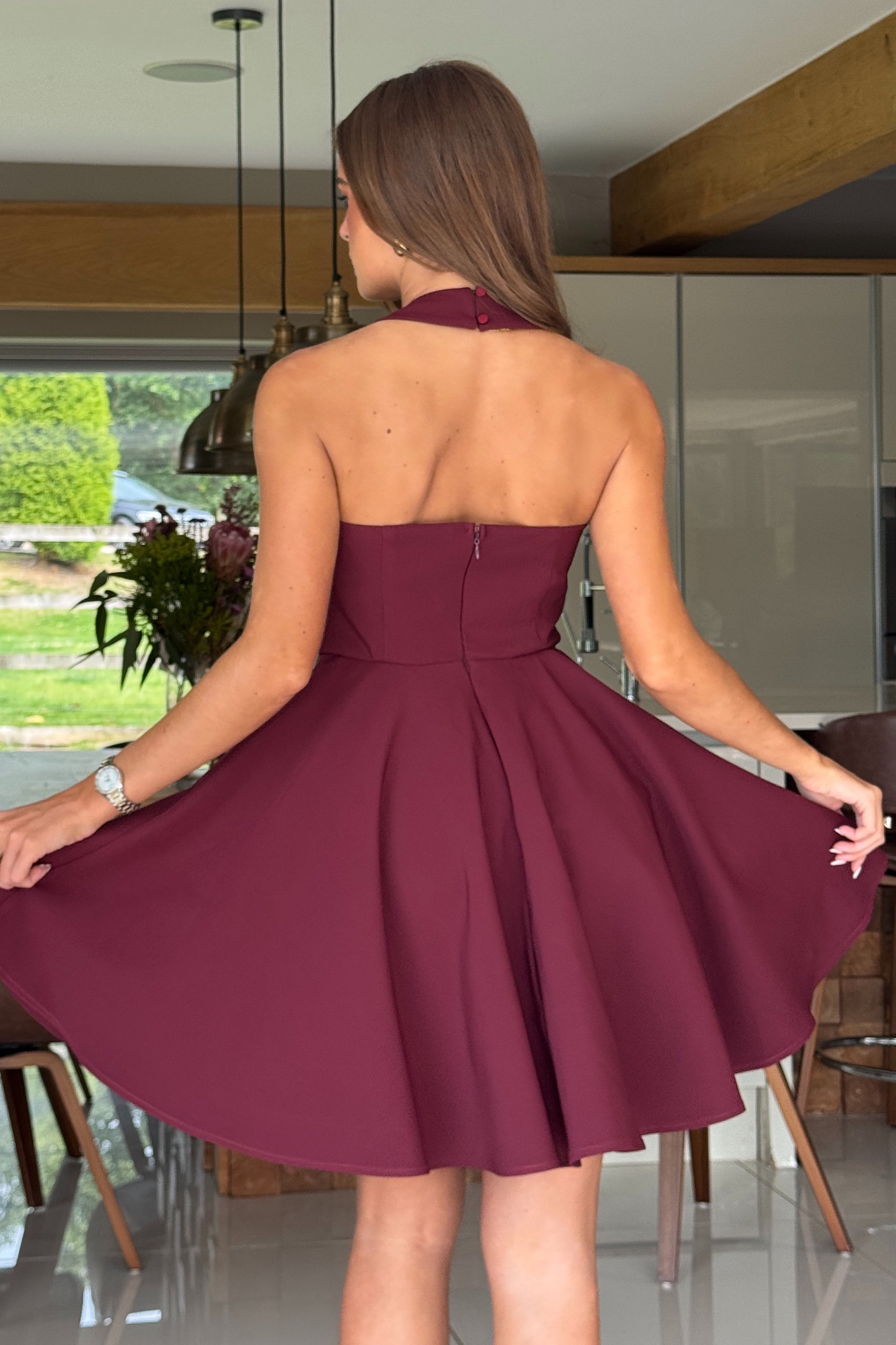Woman in a burgundy dress twirling in a modern kitchen.