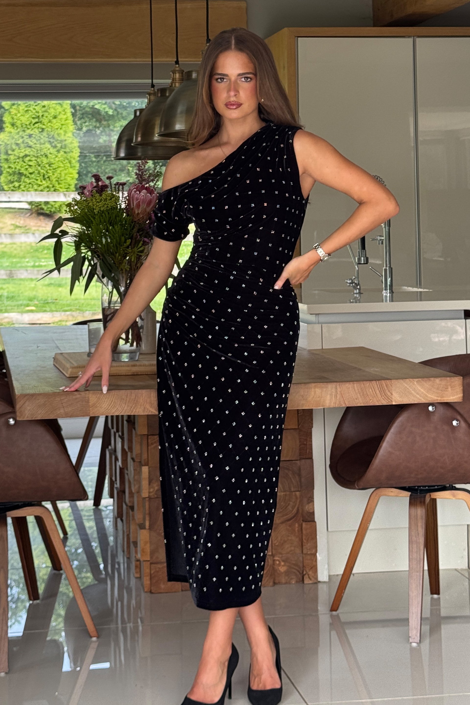 Woman in a black beaded dress standing in a modern kitchen.