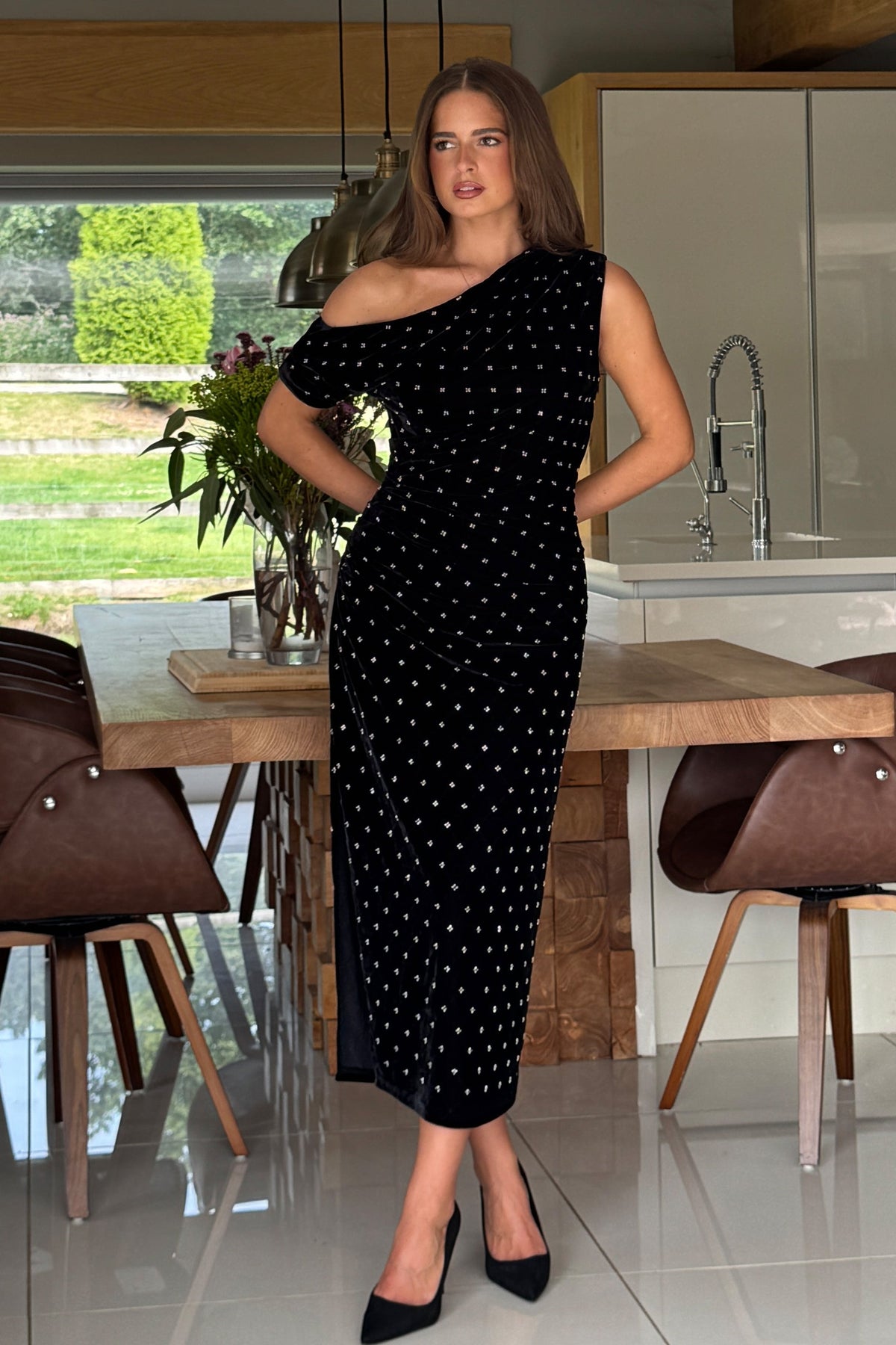 Woman in a black beaded dress standing in a modern kitchen.