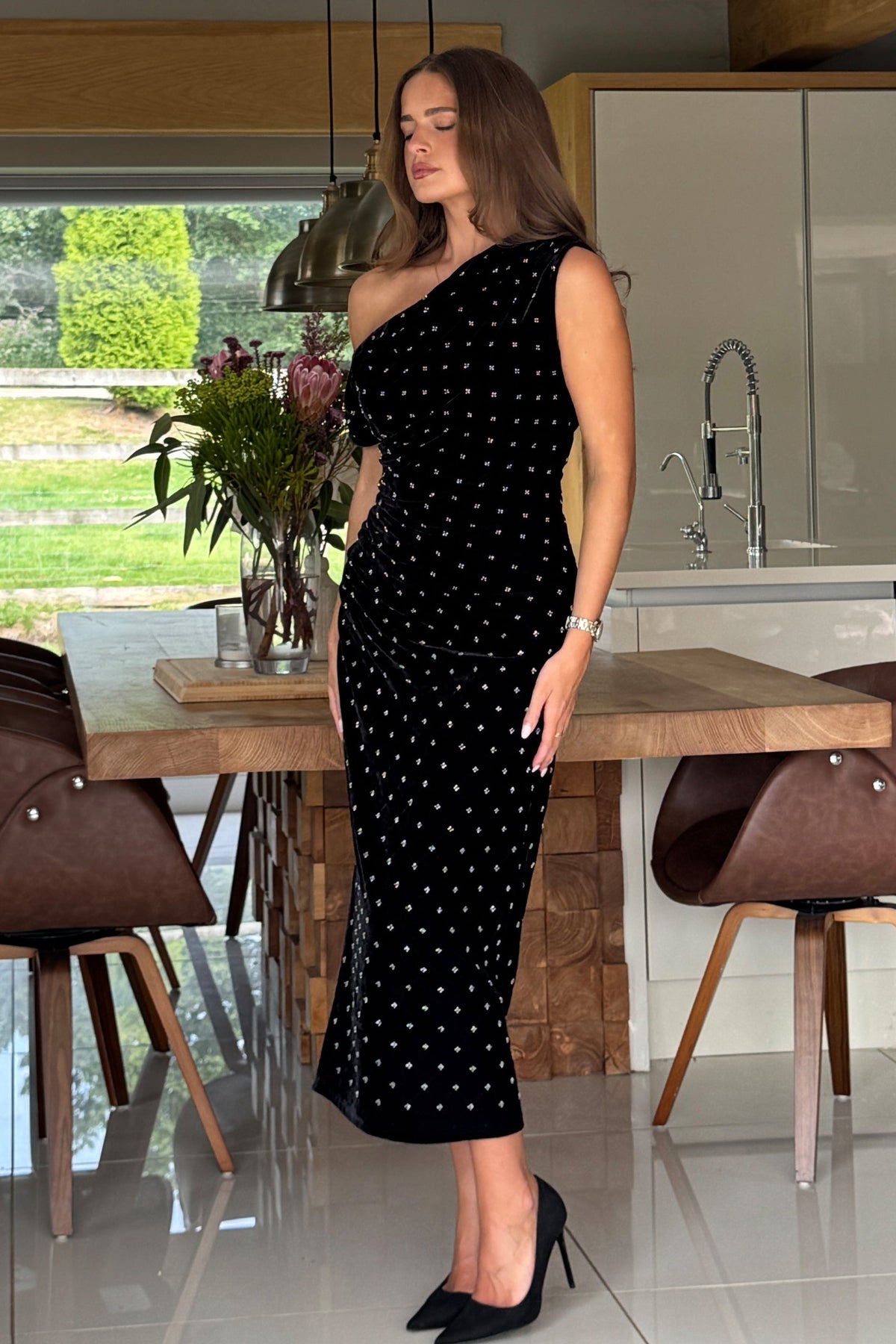Woman in a black one-shoulder dress standing in a modern kitchen.