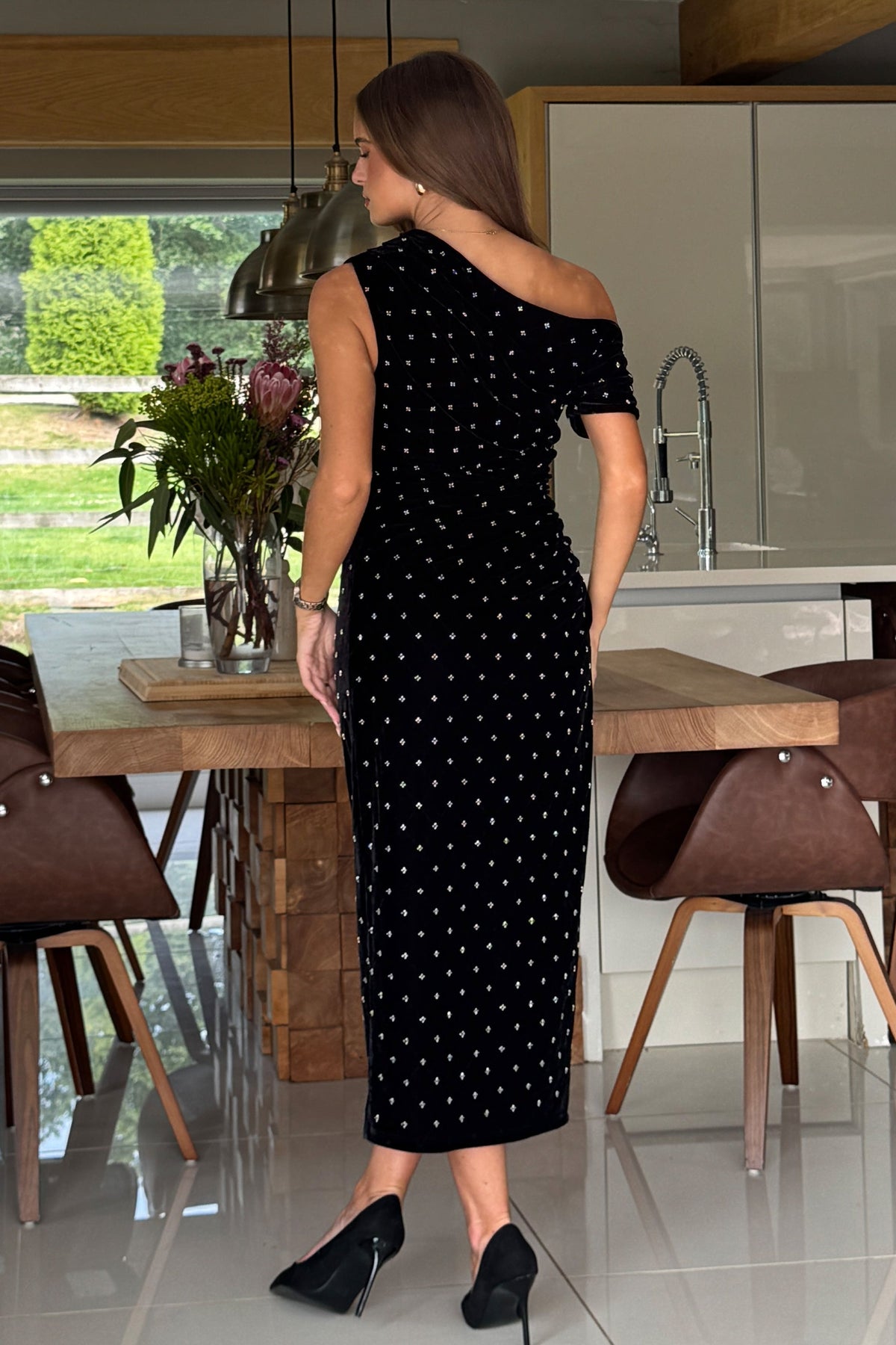 Woman in a black dress standing in a modern kitchen.