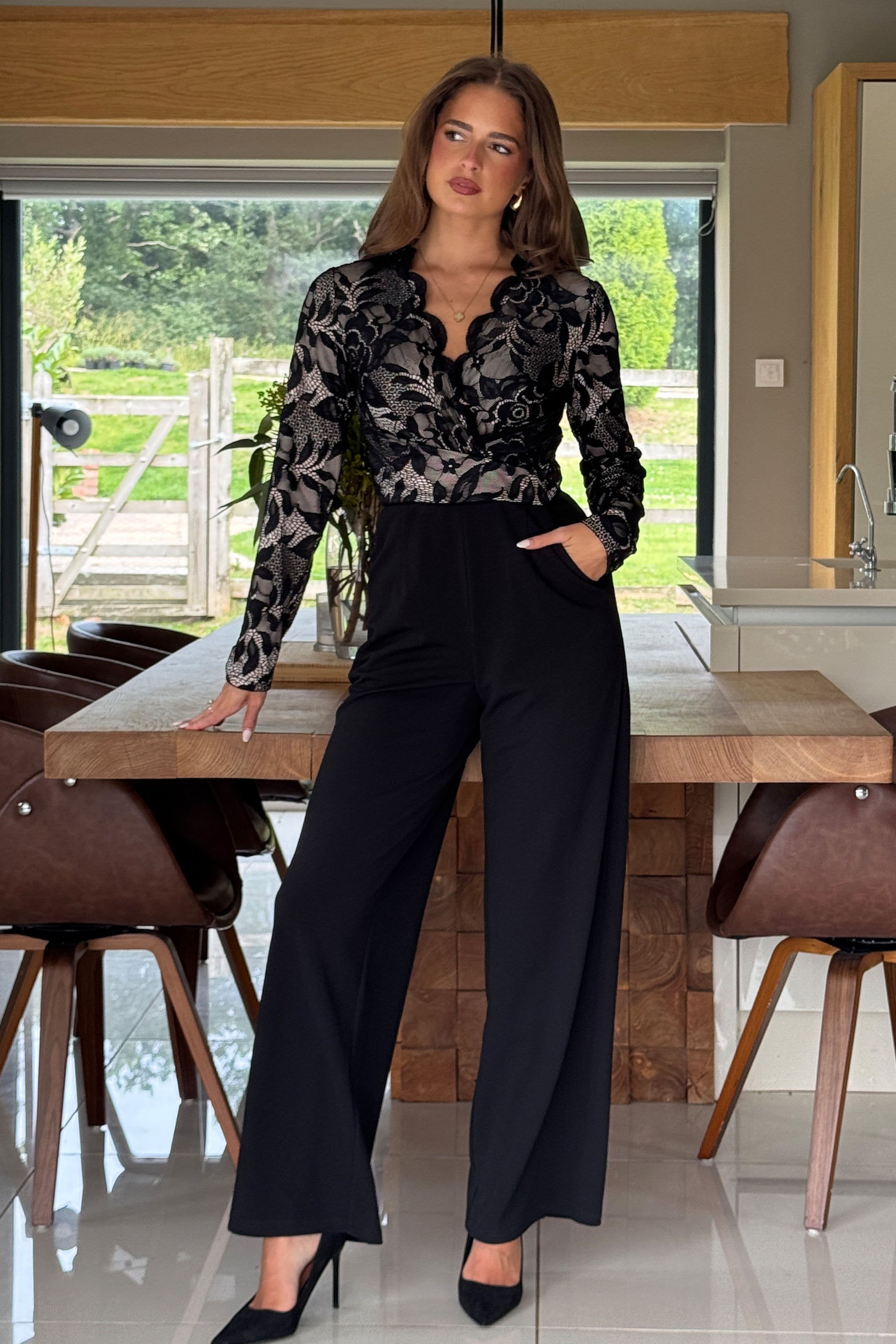 Woman in a lace top jumpsuit standing in a modern kitchen.