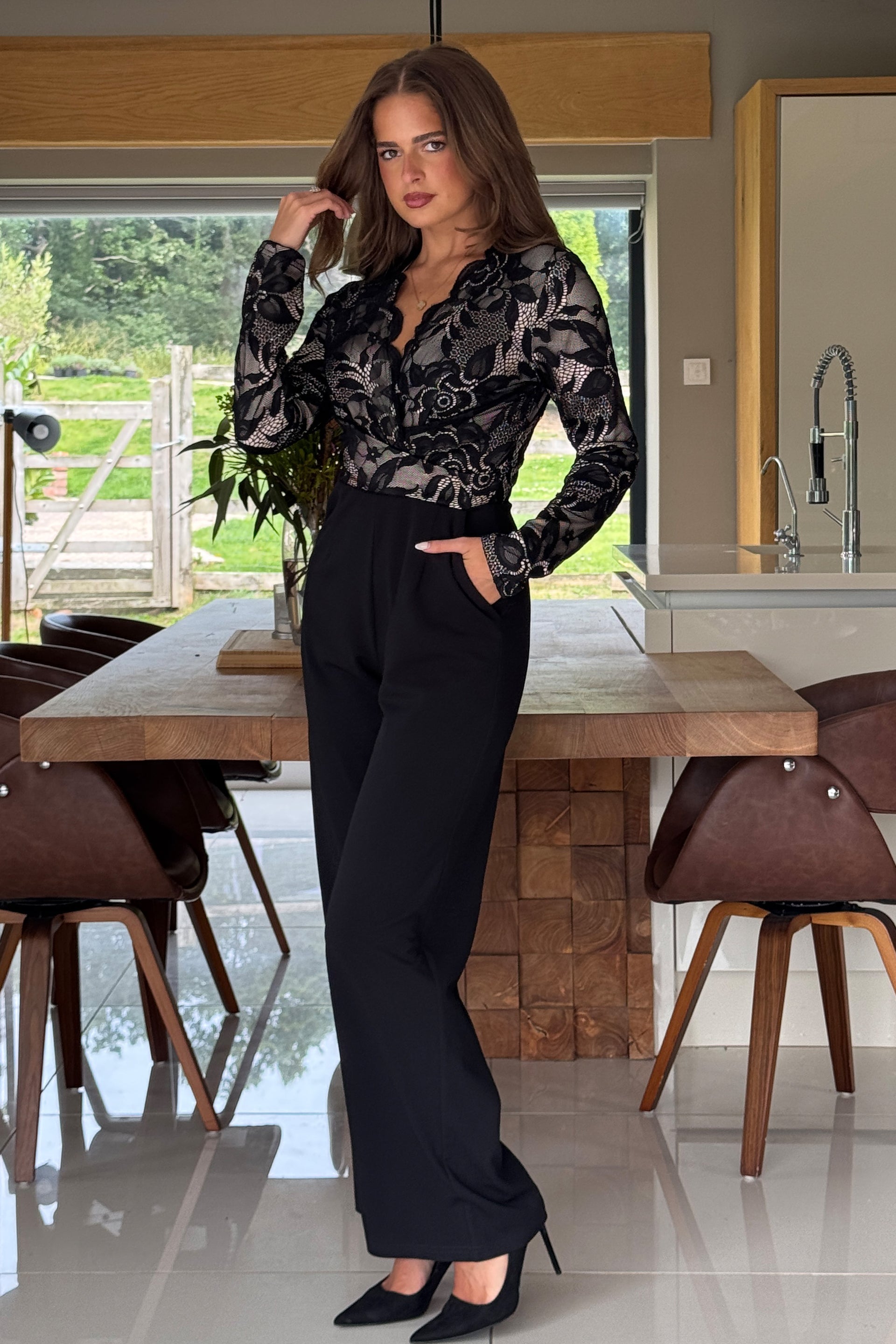 Woman in a lace top jumpsuit standing in a modern kitchen.