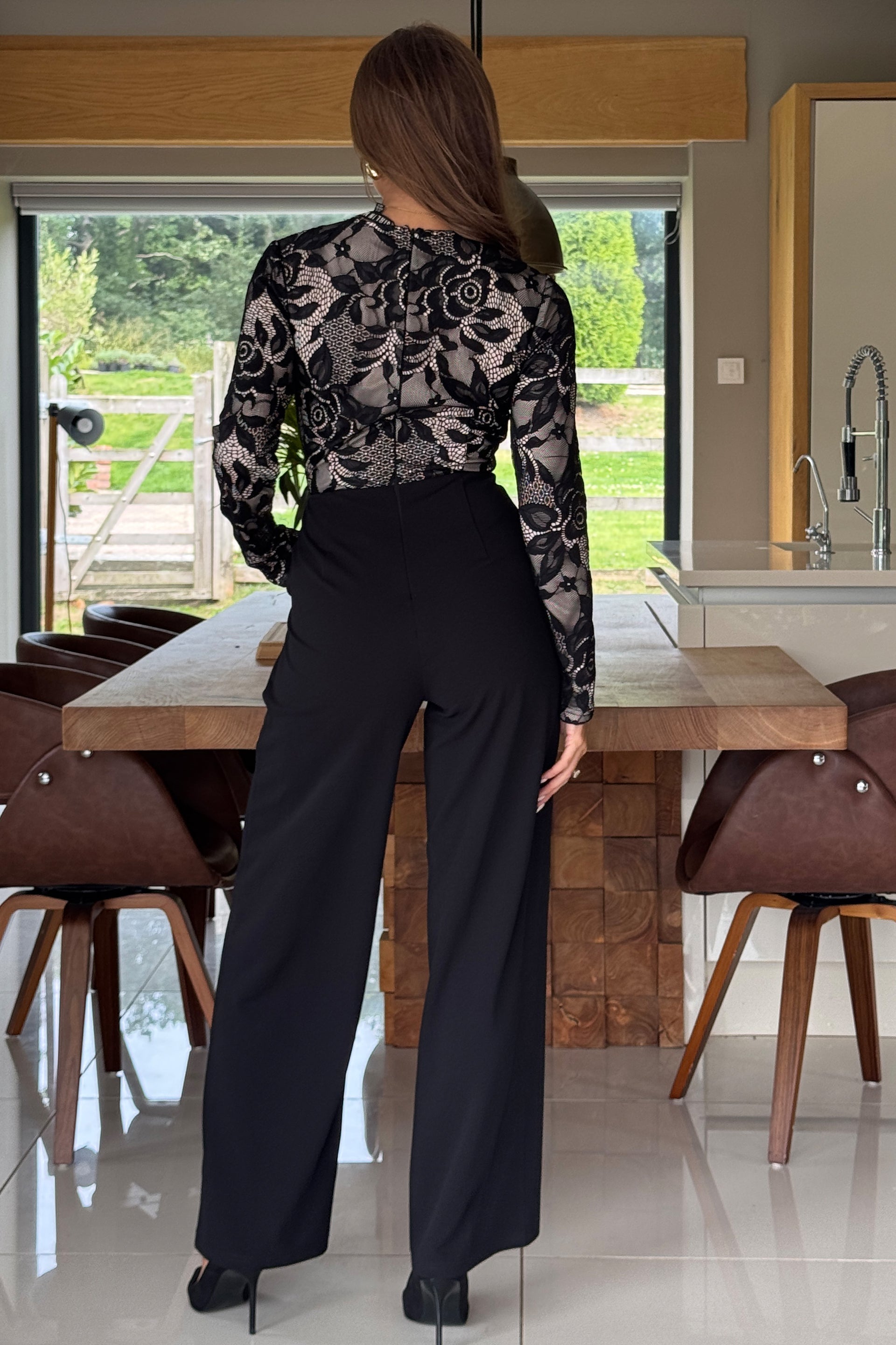 Woman in a lace top black jumpsuit standing in a modern kitchen.