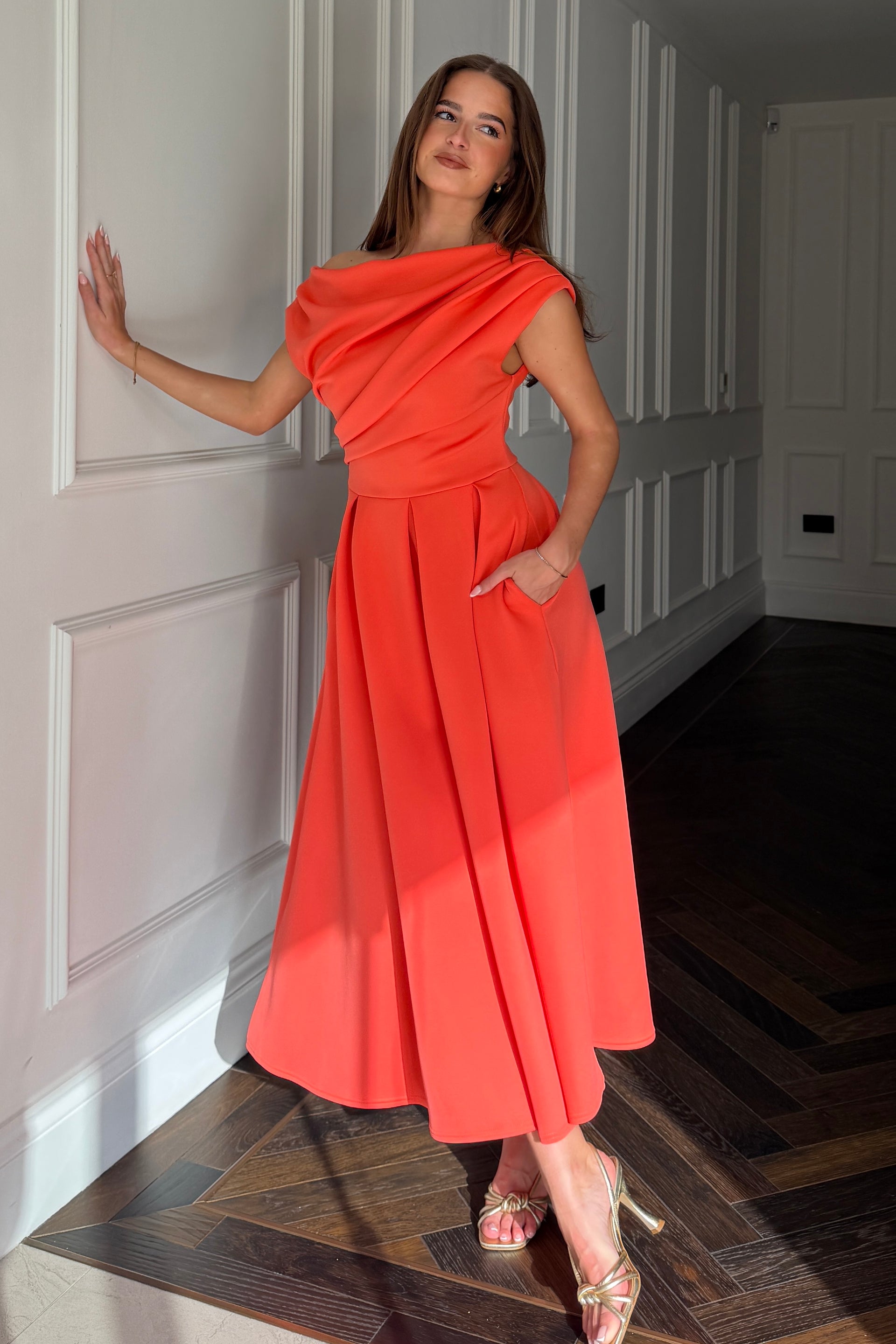 Woman in a coraldress standing in a hallway.