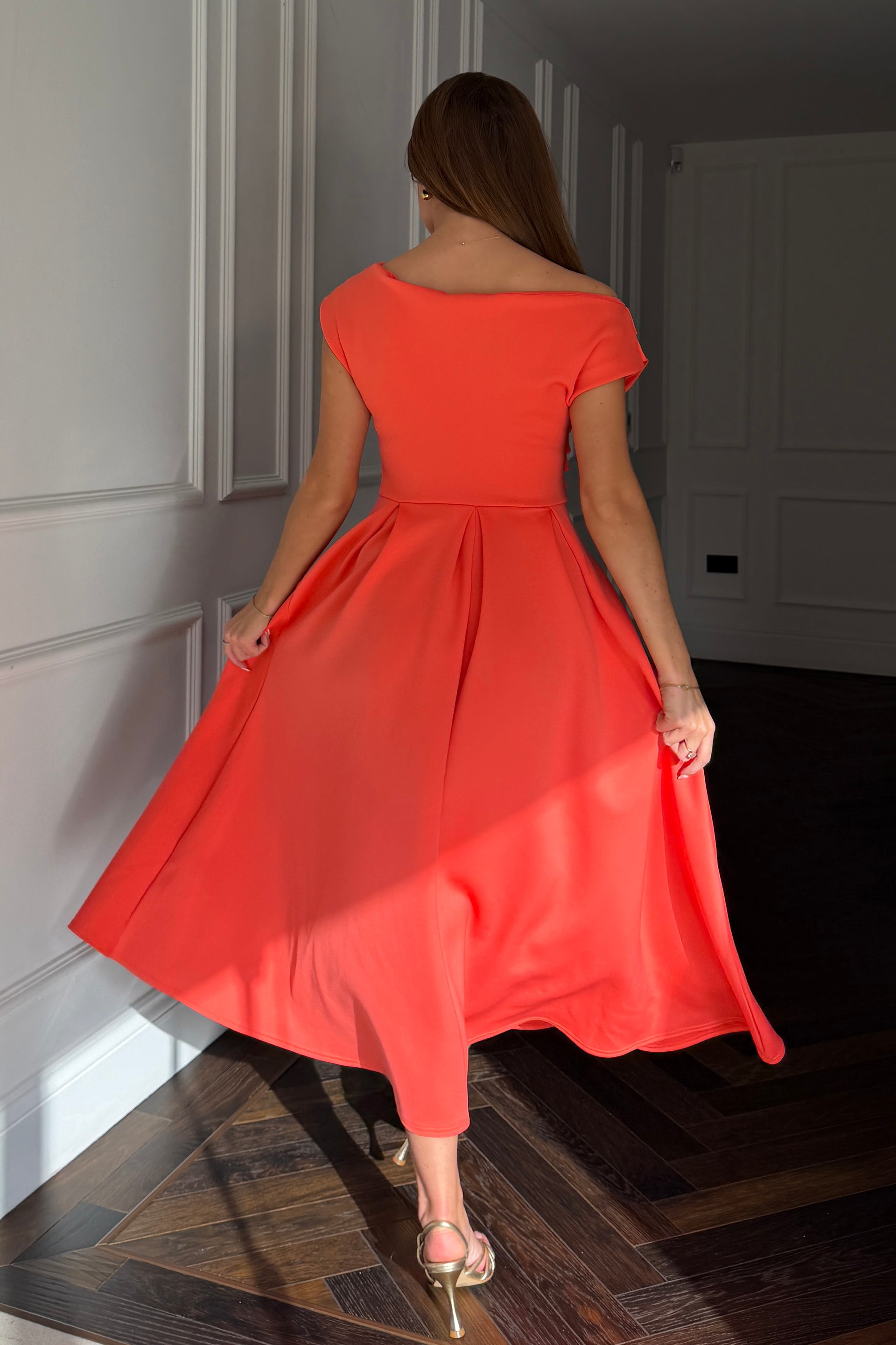Woman in a coral red dress walking away in a dimly lit room.
