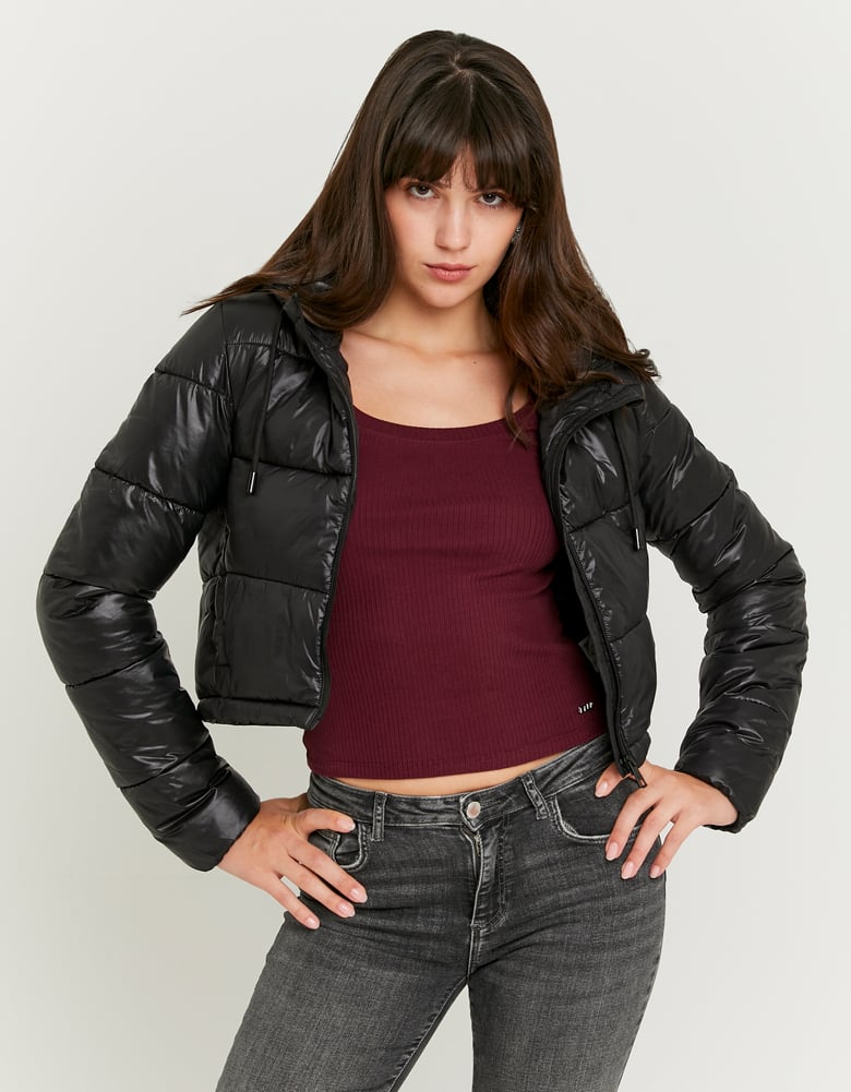 Woman wearing a black puffer jacket over a burgundy top and gray jeans on a white background