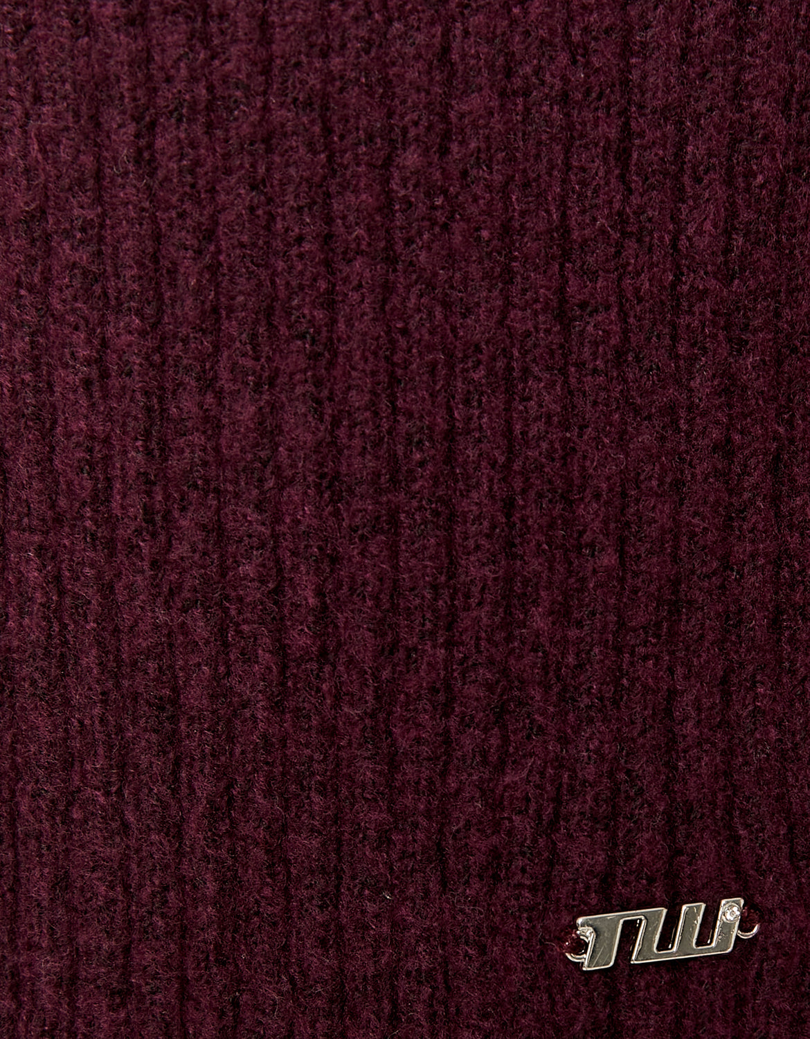 Close-up of textured maroon fabric with a brand logo in the corner.