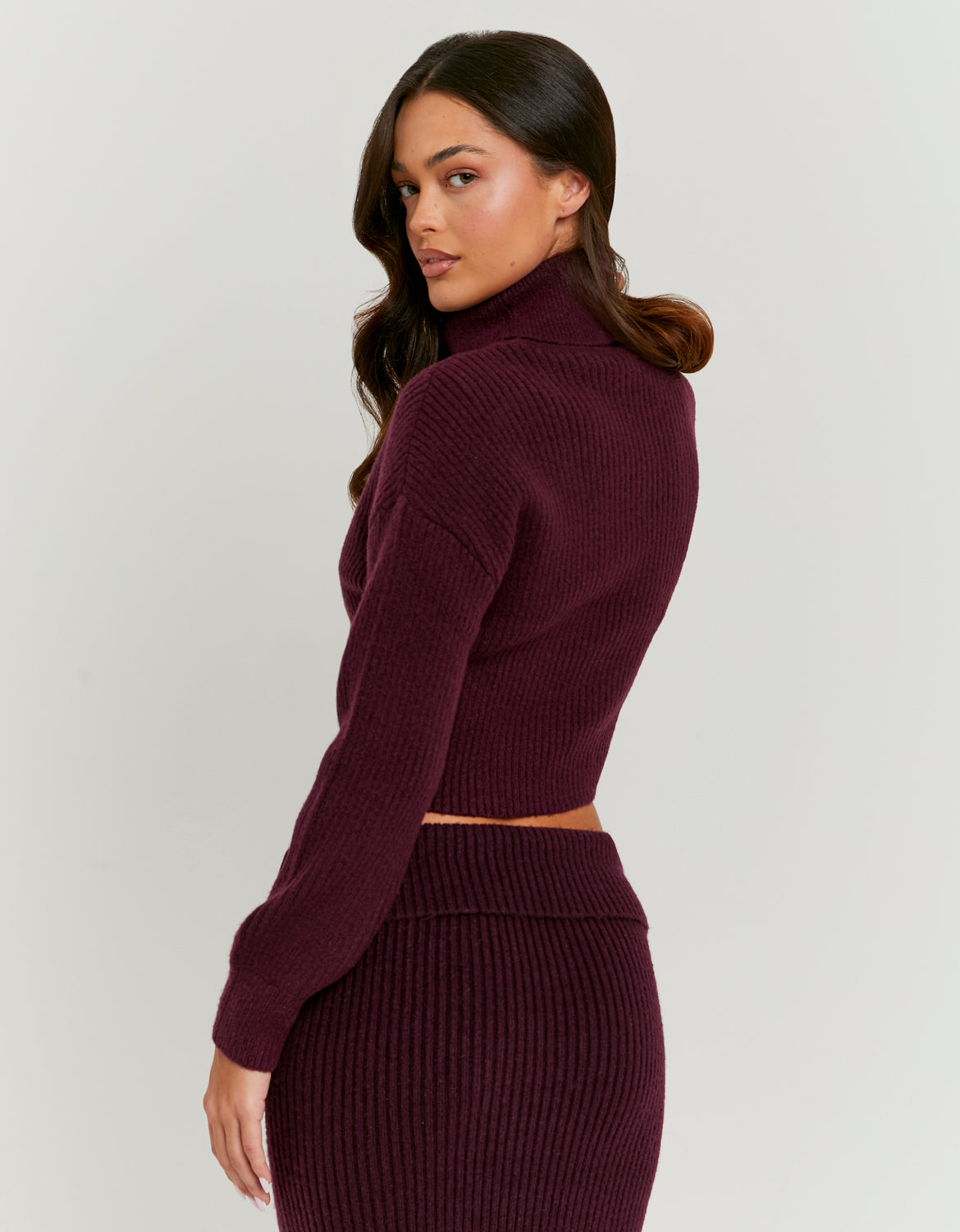 Woman wearing a maroon ribbed knit outfit on a light gray background