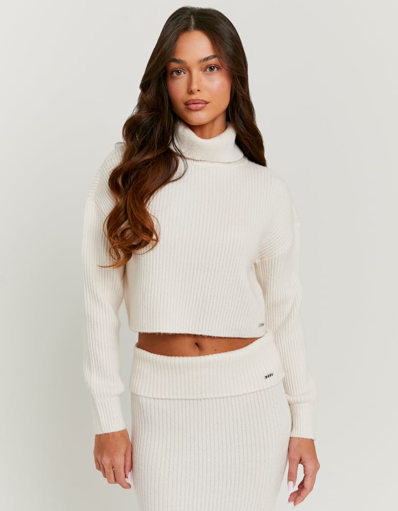 Woman wearing a white ribbed knit sweater and pants on a light gray background