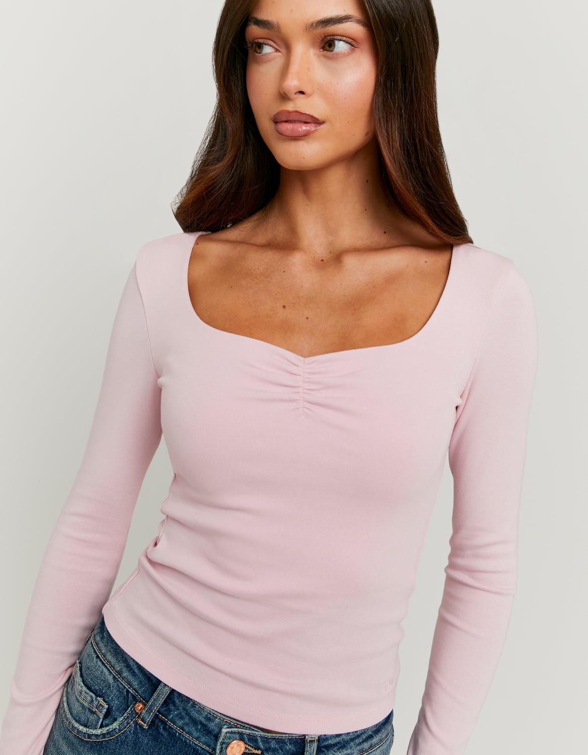 Woman wearing a light pink long-sleeve top against a plain background