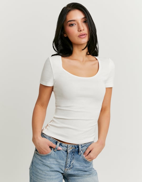 Woman wearing a white t-shirt and blue jeans against a plain background