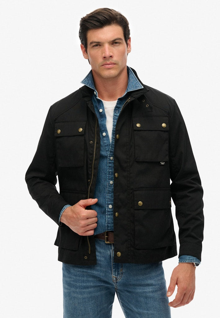 Man wearing a black jacket over a blue shirt and jeans on a white background