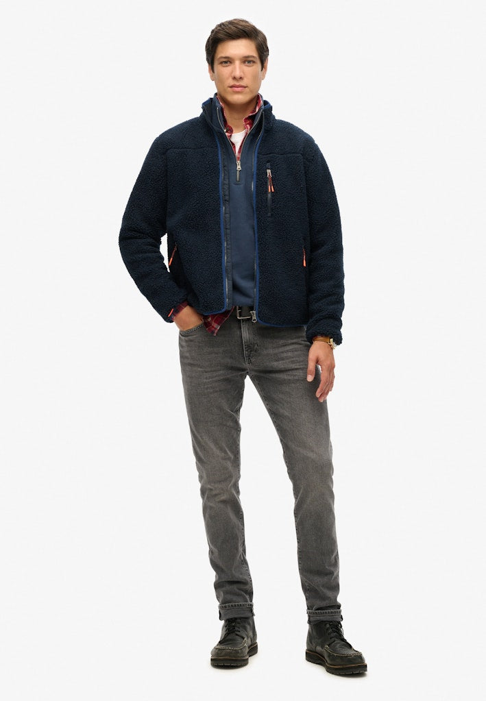 Man wearing a navy jacket, gray pants, and black boots on a white background