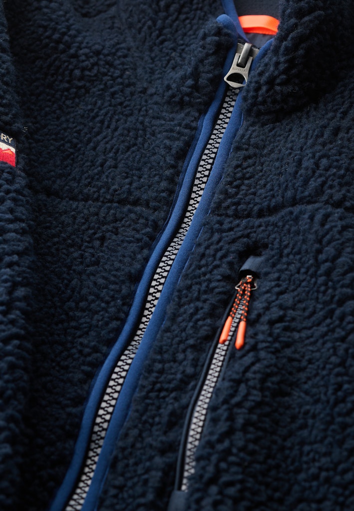 Close-up of a navy blue fleece jacket with a zipper and red accents.