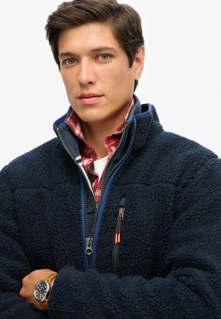 Man wearing a navy blue jacket with a plaid shirt underneath on a white background