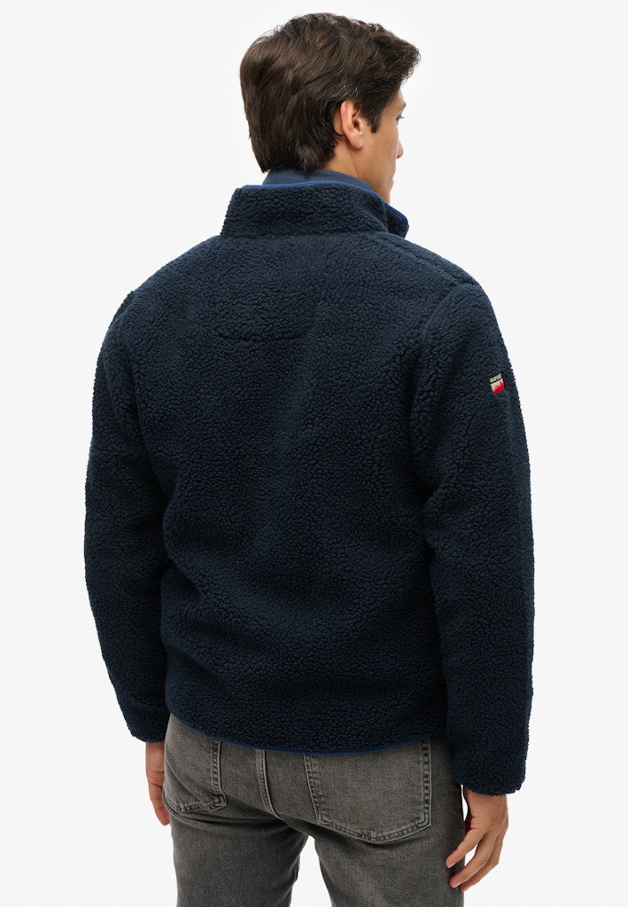 Person wearing a navy fleece jacket with a brand logo on the sleeve against a white background