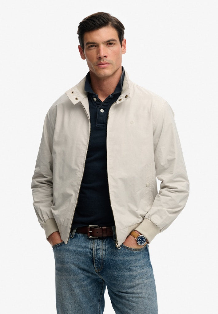 Man wearing a grey jacket over a dark shirt and blue jeans on a white background