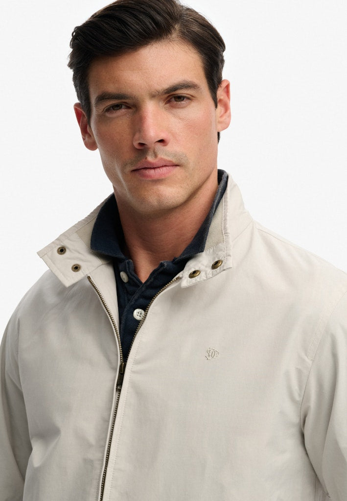 Man wearing a light gray jacket over a dark shirt on a white background