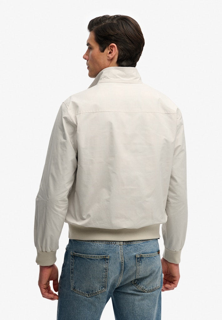 Man wearing a beige bomber jacket and blue jeans on a white background